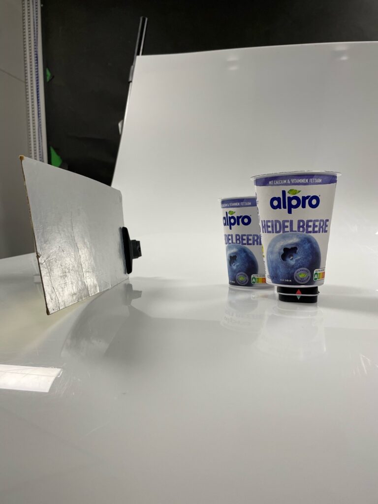 Der Aufbau von zwei Alpro Heidelbeer-Joghurts, einer steht auf einer kleinen Box, der Reflektor steht seitlich/vorne.
